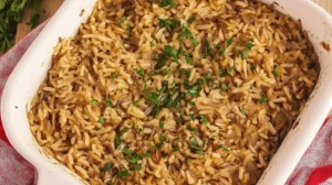 A close-up view of a baked casserole dish filled with rice and caramelized onions, resembling a frensh union soup, topped with fresh parsley.