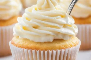 Close-up of a vanilla cupcake in a white paper liner, topped with a swirl of white frosting.