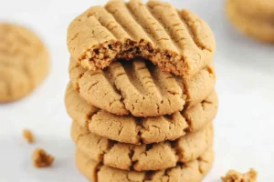 Peanut butter cookies with a cross-hatched pattern are arranged on a table with a bowl of peanut butter and a glass of milk.